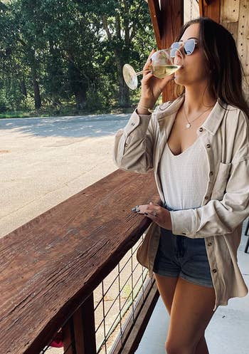 reviewer wearing the beige shacket while drinking a glass of wine
