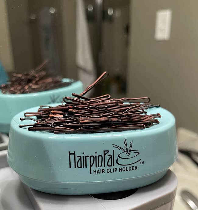 Container labeled 'HairpinPal', storing bobby pins, placed on a bathroom counter