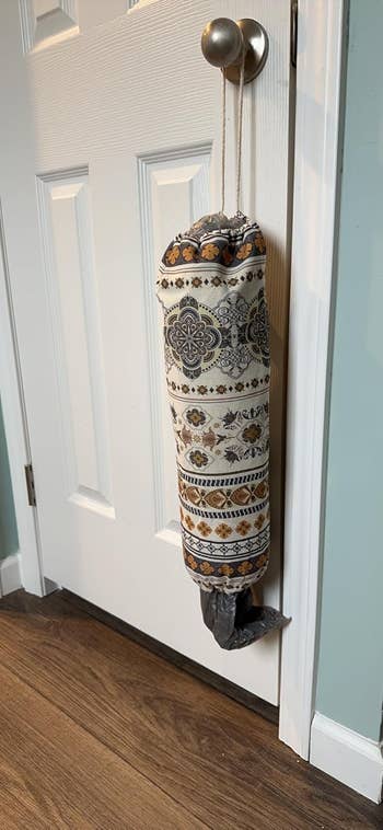Patterned cloth  container  hanging connected  a doorknob, utilized  for storing integrative  bags, with 1  container  partially visible