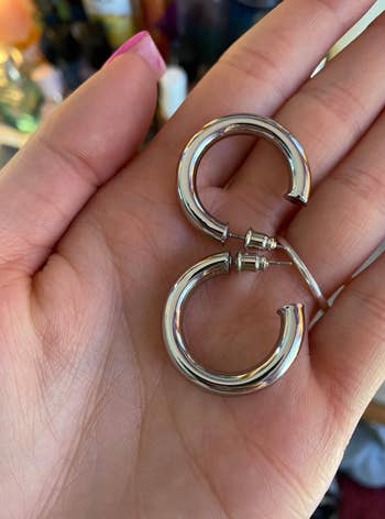 Person holding a brace  of shiny, metallic  hoop earrings
