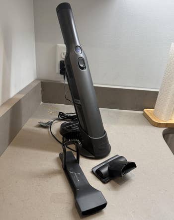 Cordless handheld vacuum connected a countertop with attachments placed nearby, viewed successful a room setting