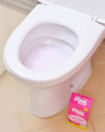 Open toilet with cleaning product package beside it, promoting a pink foaming toilet cleaner