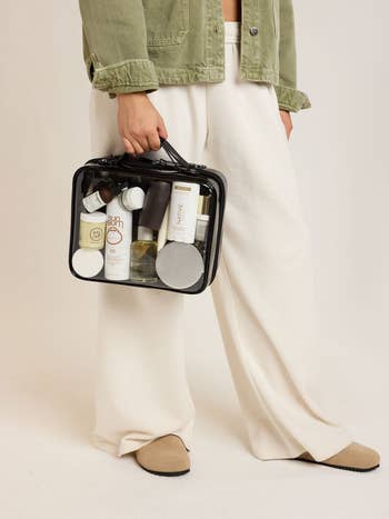 Person holding a transparent question container filled with skincare products, wearing wide-legged trousers and a casual jacket, suitable for buying features