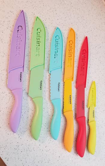 Five colorful Cuisinart knives with protective covers, ranging from large to small, arranged on a counter