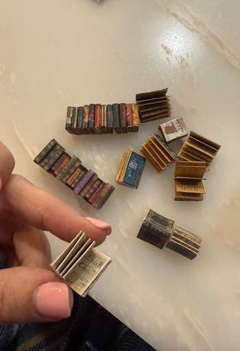 Miniature books with intricate covers and disposable   text, held successful  a person's hand, displayed connected  a table, featured successful  a buying  article