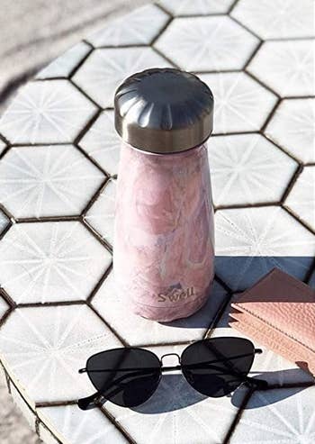 The geode rose-colored bottle on a counter and by a pair of sunglasses