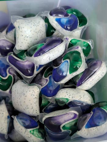 A instrumentality filled with assorted detergent pods, featuring speckled achromatic and sections of gel
