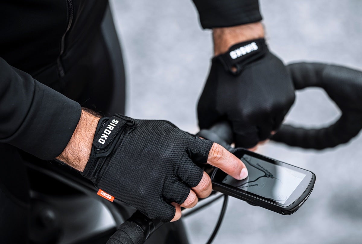 model wearing Siroko fingerless bike gloves, using touchscreen on cell phone on bike