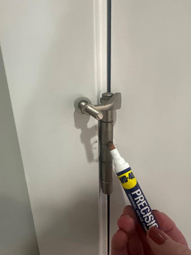 Person utilizing a WD-40 pen connected a doorway hinge for maintenance