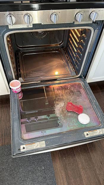 an oven door partially cleaned and shiny after using the pink stuff