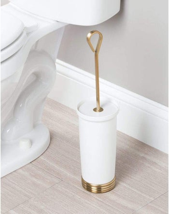 the white and gold toilet brush holder in a bathroom