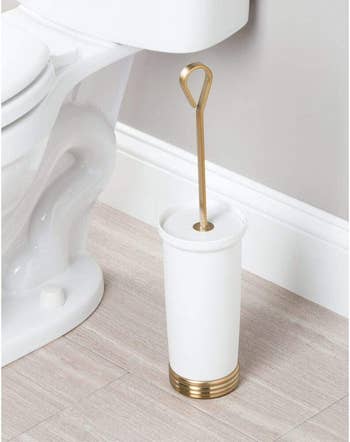 the white and gold toilet brush holder in a bathroom