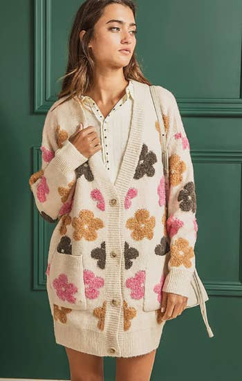 a model in a long tan cardigan with plush flowers on it
