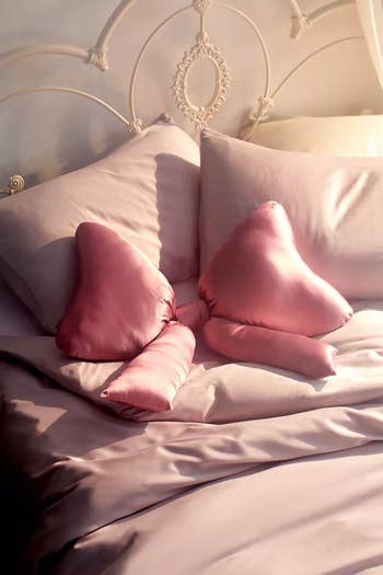 Assorted satin decorative pillows on a bed, including two heart-shaped and one roll-style. Perfect for home decor shopping