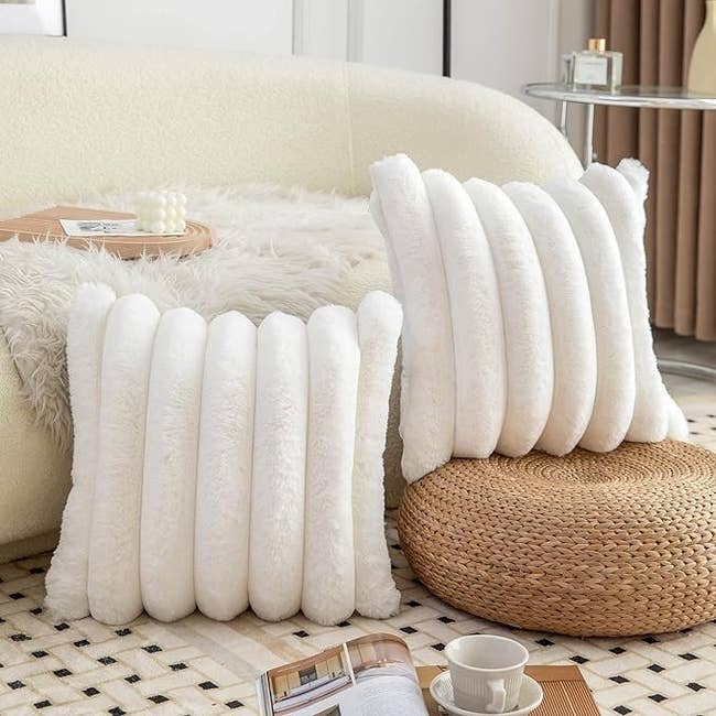 Plush white cushions arranged vertically on a sofa in a cozy room setup with a wicker ottoman