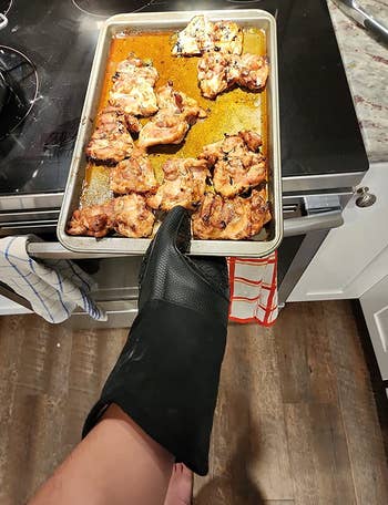 reviewer wearing the black oven mitt while holding a hot sheet tray of food