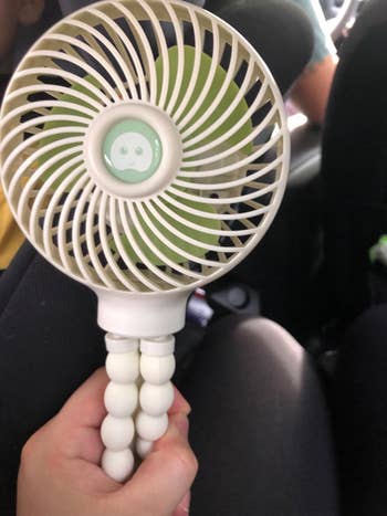 A manus  holds a portable instrumentality   with a smiling look   plan  connected  its center, perfect  for on-the-go cooling