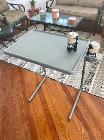 Small gray tray table with two legs holding a can of coke 