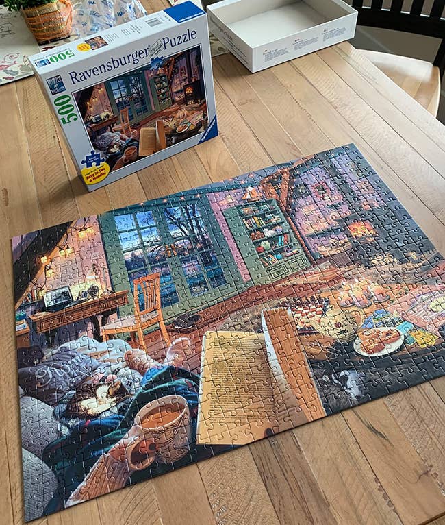 reviewer photo of the completed cozy retreat puzzle in front of the puzzle box