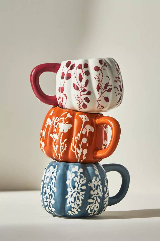 a stack of pumpkin shaped mugs in different colors with floral designs on each