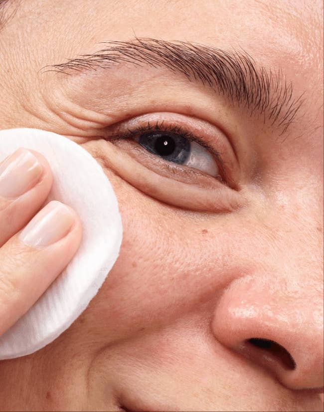 Close-up of a person removing makeup with a cotton pad from under their eye