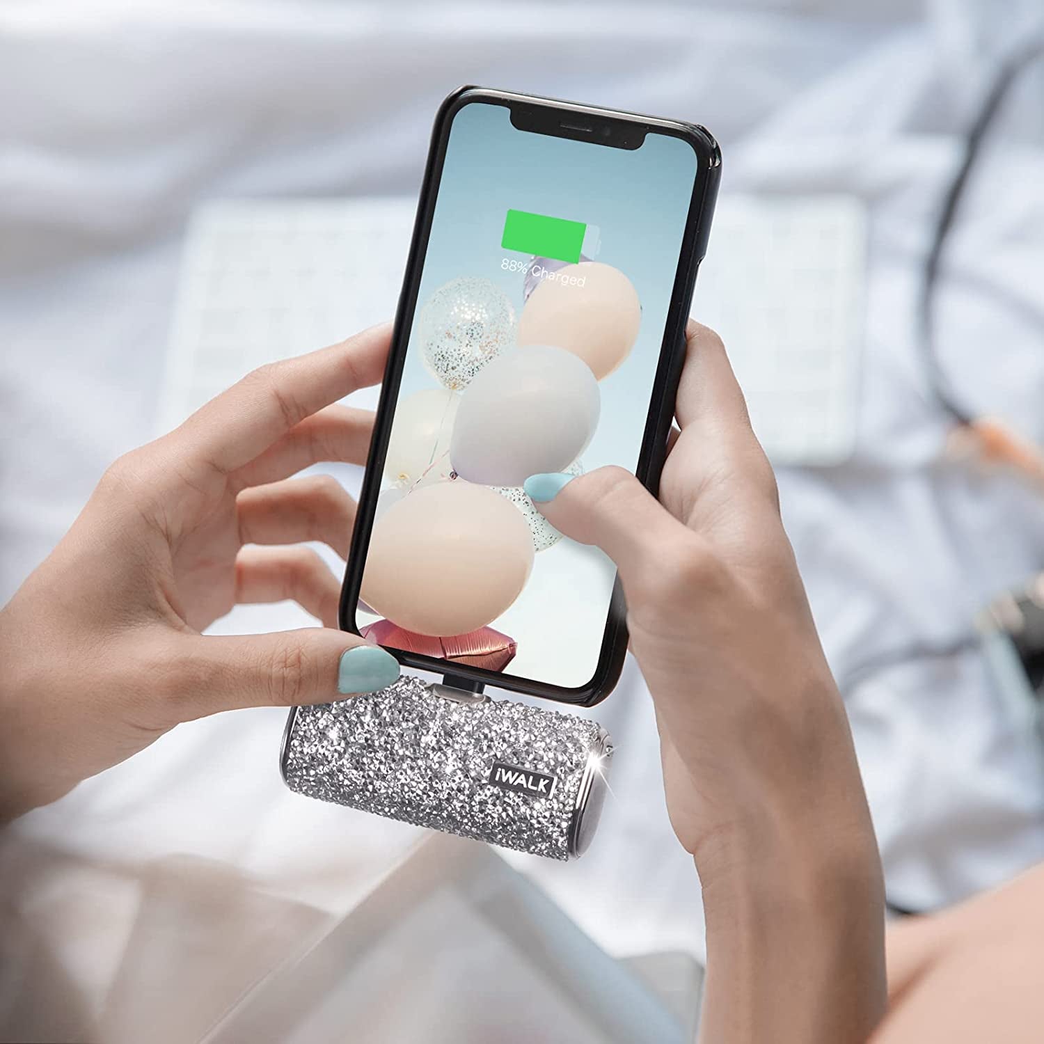 Model texting on phone with small silver glittery cylinder-shaped charger attached to bottom