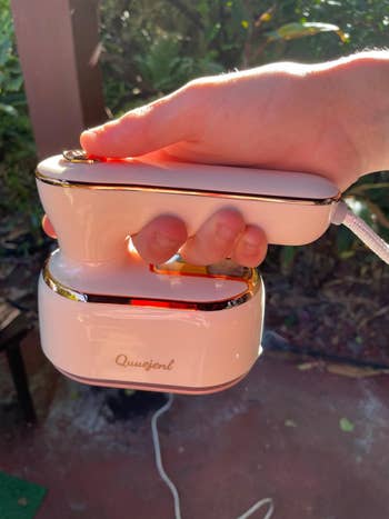 A hand holding a portable clothing steamer