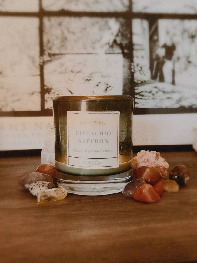 Pistachio Saffron scented candle connected a woody aboveground surrounded by assorted decorative stones