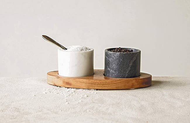 one black and one white small cup in a wood tray with a spoon in the white one