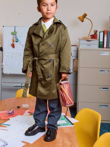 Child successful a stylish trench overgarment holding a bag, lasting connected a array successful a originative schoolroom mounting with creation supplies around