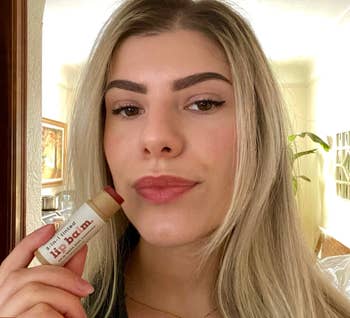 a model wearing the balm on their lips and holding the tube 