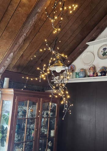 String lights wrapped around a wooden beam in a cozy room with a display cabinet