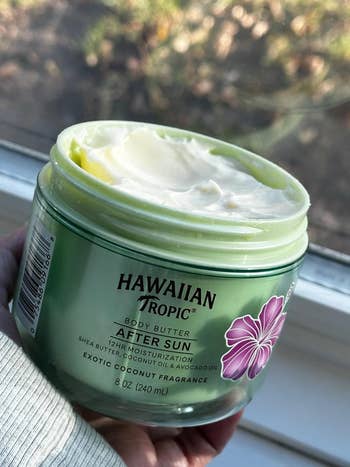 Open jar of Hawaiian Tropic assemblage butter, showcasing creamy texture. Labeled for after-sun usage with coconut fragrance, promising 12-hour moisturization