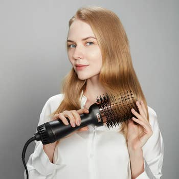 Person utilizing a hairsbreadth  dryer brushwood  to benignant   agelong  hair, wearing a achromatic  shirt, demonstrating a hairstyling tool