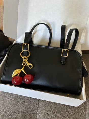 Black leather handbag with golden  accents and a cherry keychain, placed successful  an unfastened  box