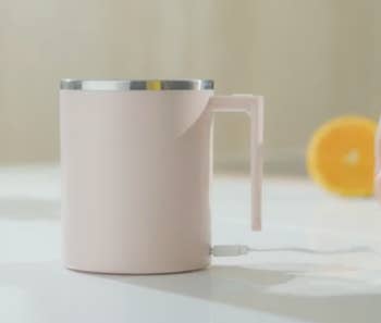 A pale pink mug with a handle and a stainless steel rim 