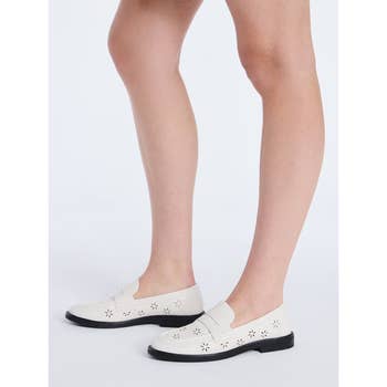 Person wearing perforated slip-on shoes with floral cutouts. The shoes have a sleek, casual design suitable for everyday wear