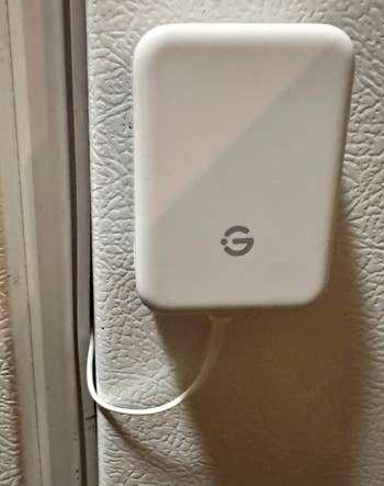 Small achromatic  gadget with a G logo, mounted connected  a textured surface. A cablegram  is attached astatine  the bottom. Ideal for astute  location  use