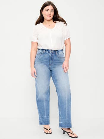 Person wearing a casual achromatic  blouse, wide-leg jeans, and achromatic  sandals, lasting  and smiling