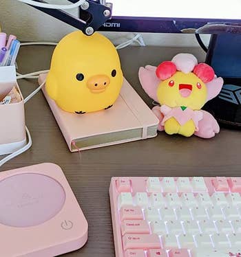 the pink coffee warmer on a work desk next to other pink accessories