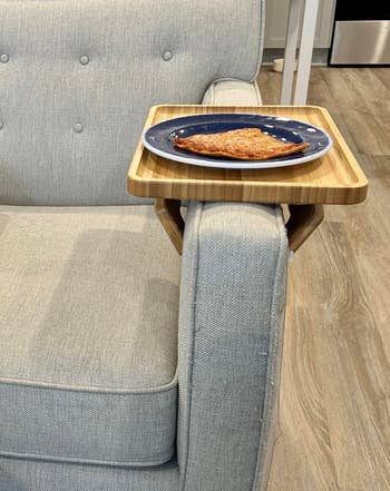 Couch with a woody armrest tray holding a bluish sheet with a portion of toast, highlighting convenient location accessory for dining