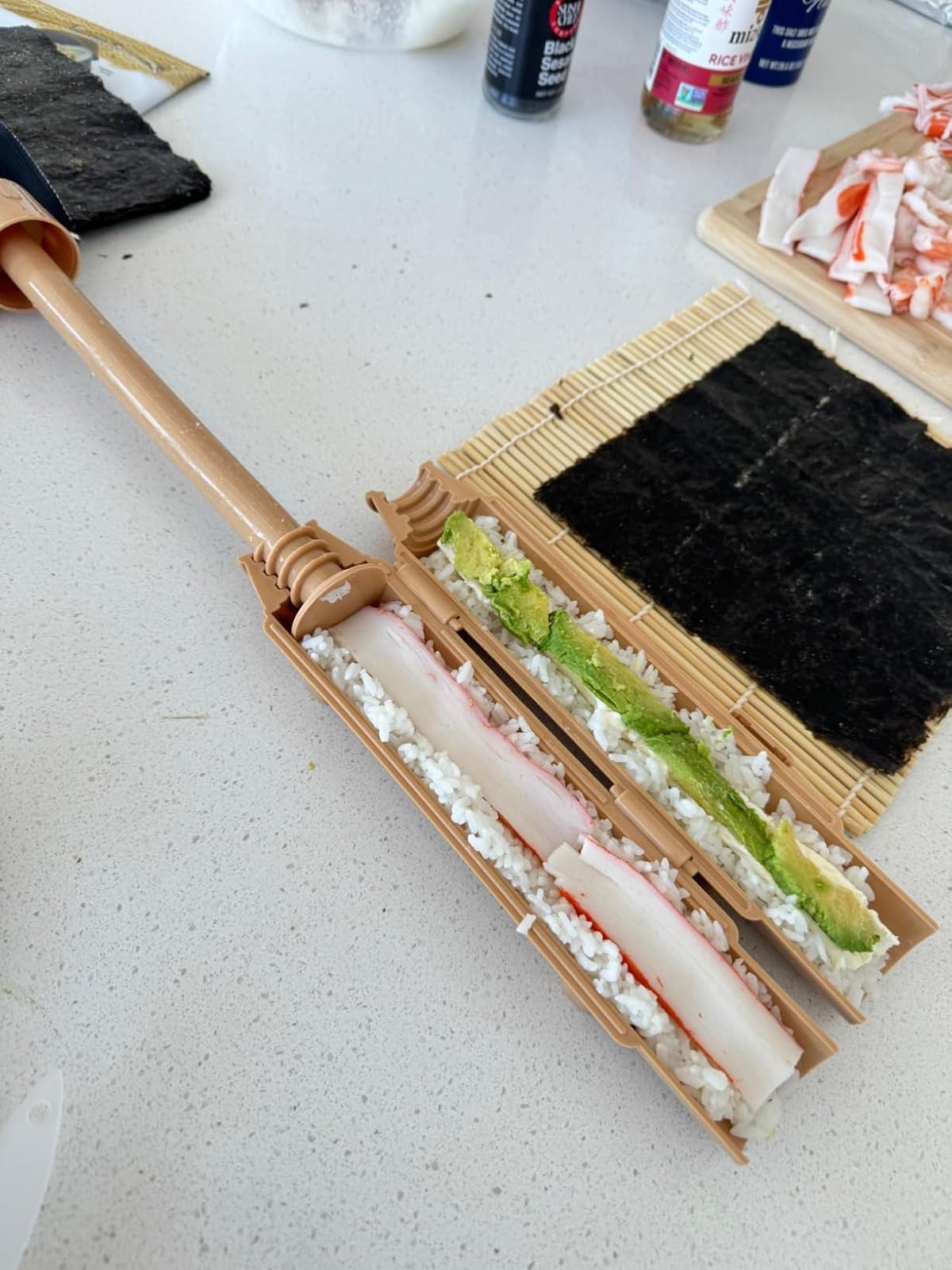 Sushi-making kit connected  a antagonistic  with crab, rice, and wasabi, showing sushi rolled with a bamboo mat and sushi bazooka tool