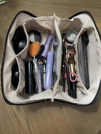 An open makeup bag with various beauty products, including brushes, compacts, and lipsticks, organized in compartments