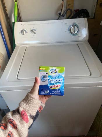Person holding a box of washing machine cleaner in front of a washing machine