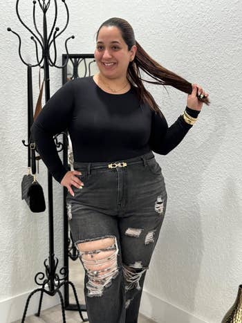 reviewer poses successful  distressed jeans and a achromatic  long-sleeve shirt, and a skinny achromatic  belt.