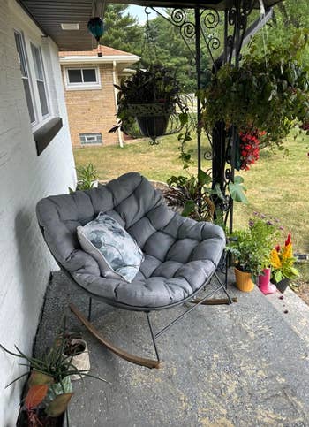 Cozy rocking seat  with a cushion connected  a porch, surrounded by lush plants and flowers, perfect  for outdoor relaxation