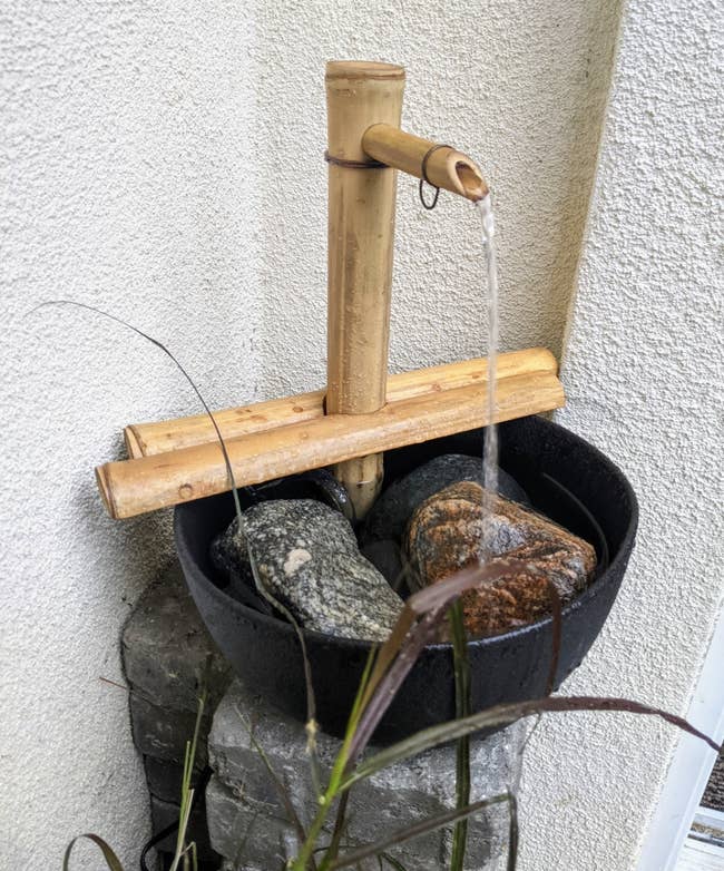 Bamboo h2o  diagnostic   with stones successful  a achromatic  basin, placed against a textured wall
