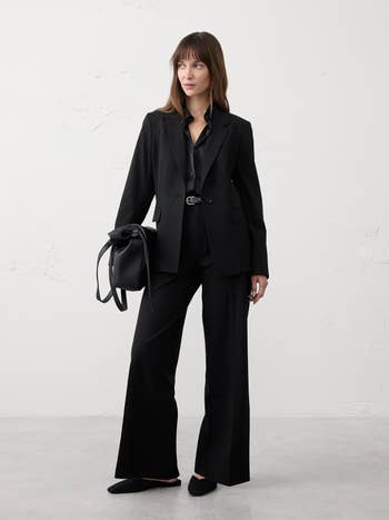 A idiosyncratic   successful  a stylish achromatic  suit   with wide-leg pants and a achromatic  blouse, holding a achromatic  bag