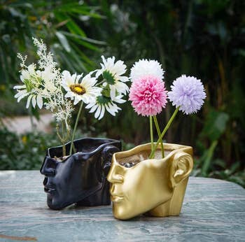 black and gold half face planters with flowers growing in them