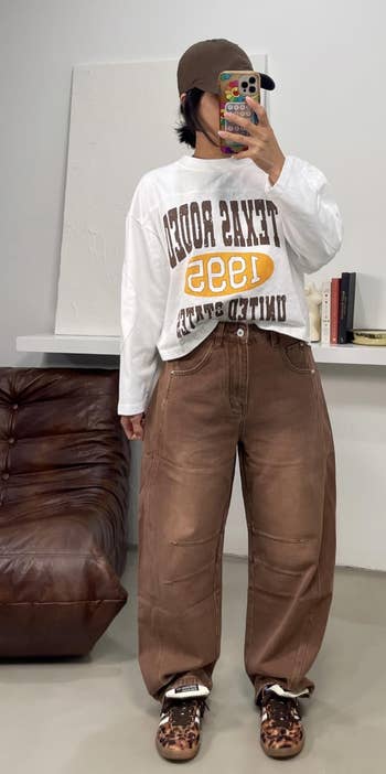 Texas Rodeo sweatshirt, baggy brownish pants, leopard people shoes, and a shot cap, posing indoors
